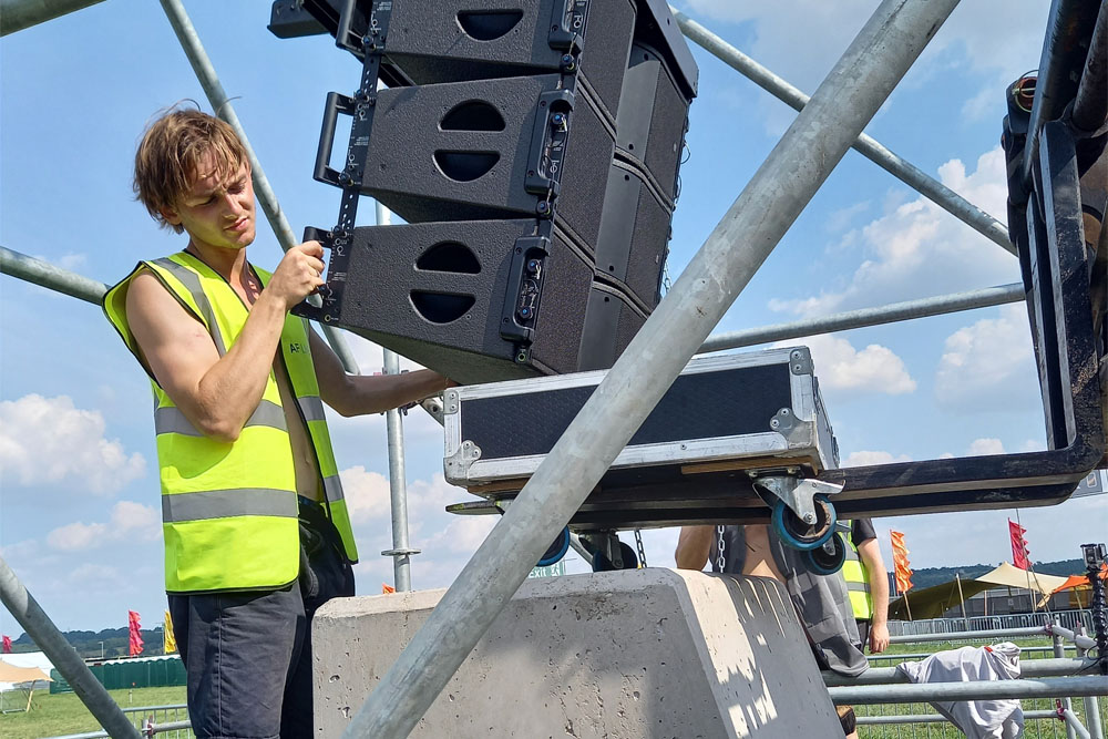 A student in a high-vis jacket rigging a speaker array at a festival