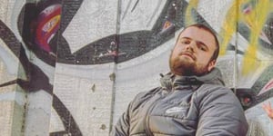Connor Paul posing in front of a concrete wall covered in street art