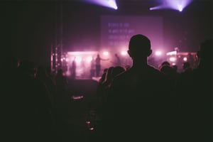 A dark photo taken from a live performance that shows the silhouette of a person watching the stage