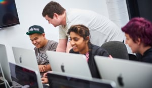 A tutor helping students produce music on an iMac computer