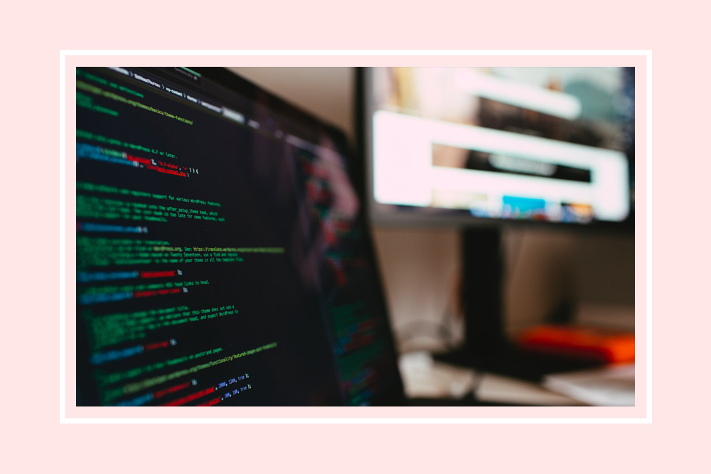 A laptop on a desk with code on the screen and a second monitor in the background