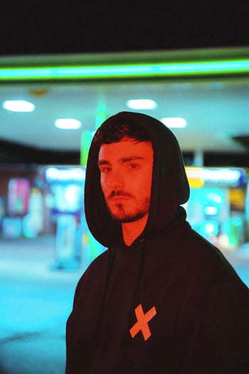 Tom Westy in a hoodie with an out of focus petrol station behind him